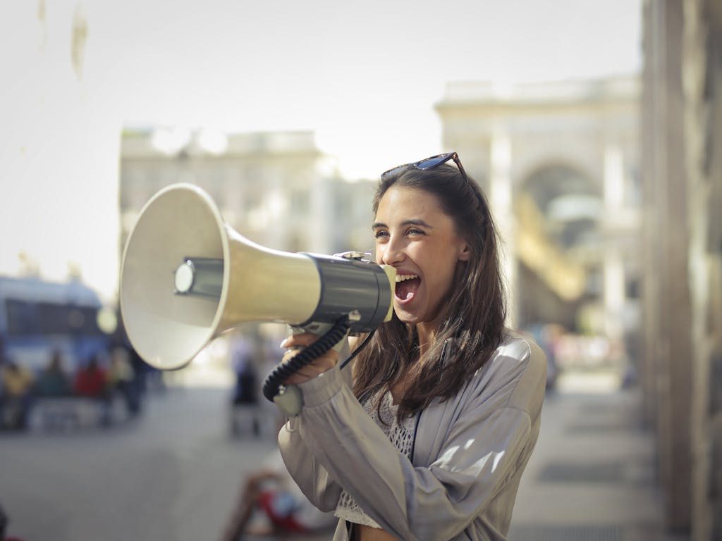 Cheerful young woman screaming into megaphone